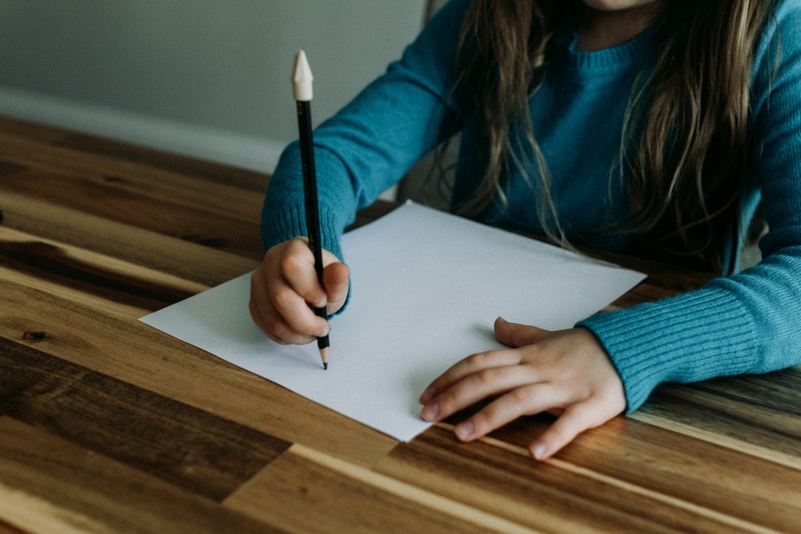 Criança a escrever numa folha de papel à mesa