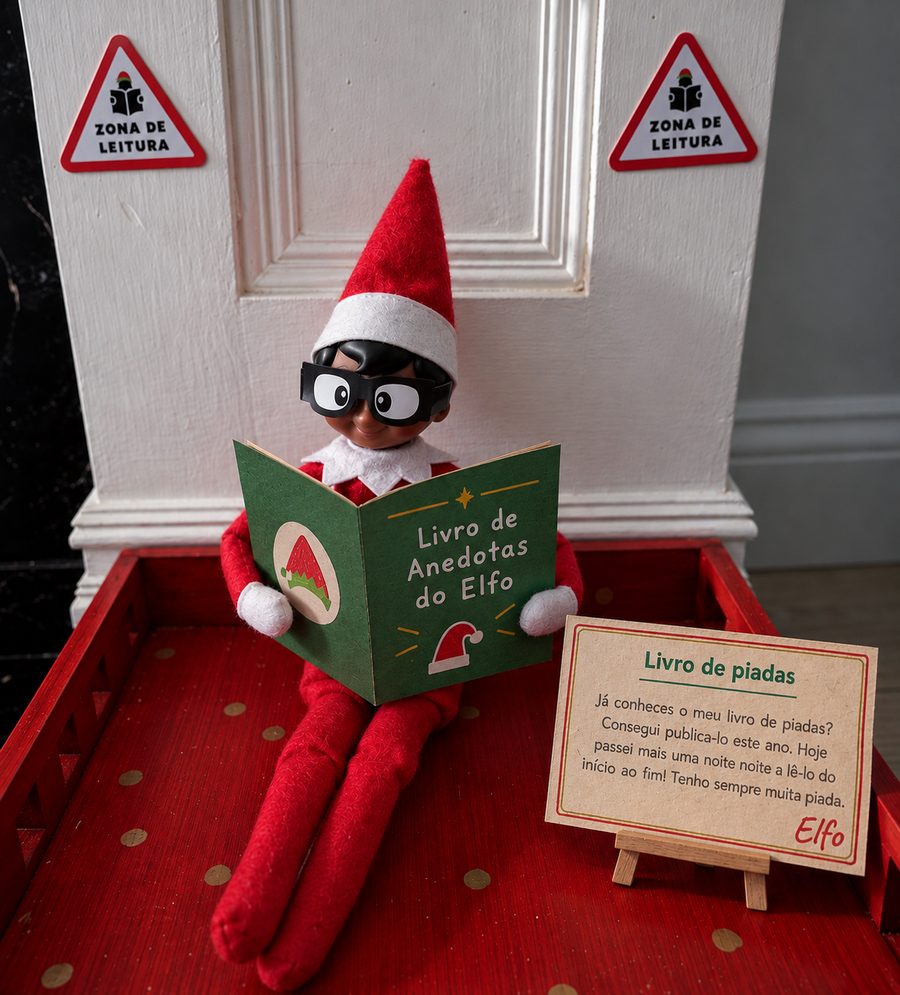 Elfo de Natal de óculos a ler o «Livro de Anedotas do Elfo» numa zona de leitura